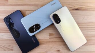 Three smartphones in different colors on a wooden surface