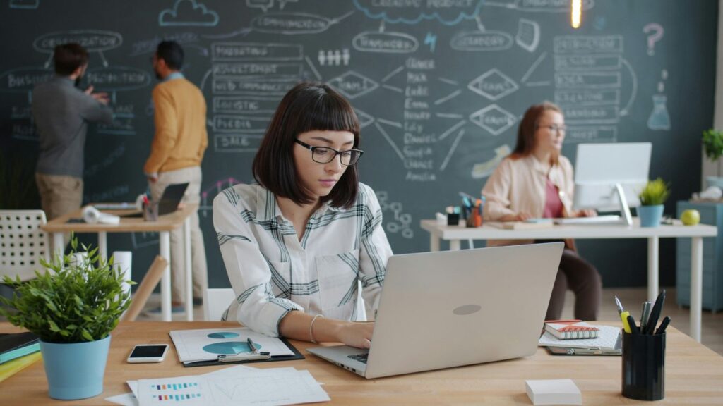 Woman working on laptop in modern office with team.