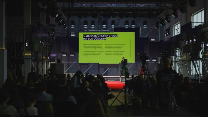 A speaker presents on a large stage with a screen.