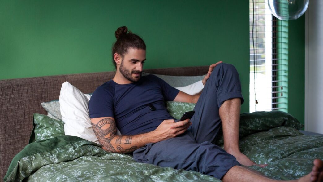 a man sitting on a bed looking at his cell phone