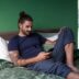 a man sitting on a bed looking at his cell phone
