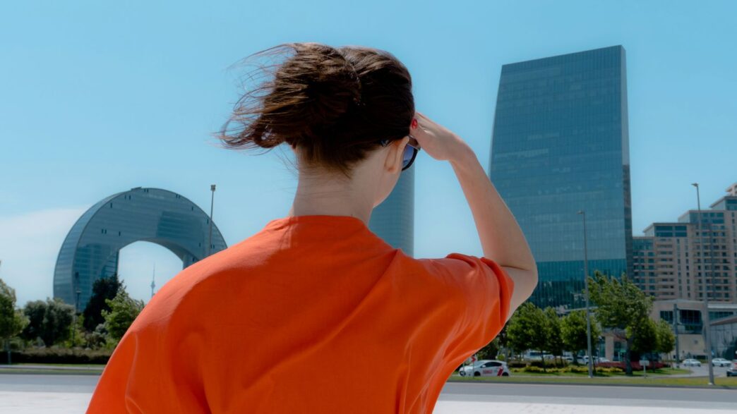 Woman in orange shirt looking at modern city buildings