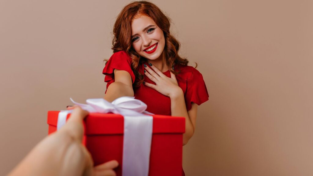 a woman holding a red gift box with a white ribbon