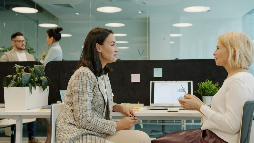 Two women talking at a desk in an office.