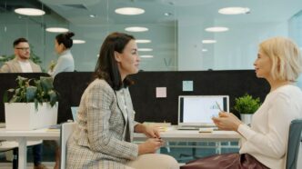Two women talking at a desk in an office.