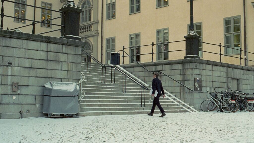 A man walking down a snow covered street next to a building