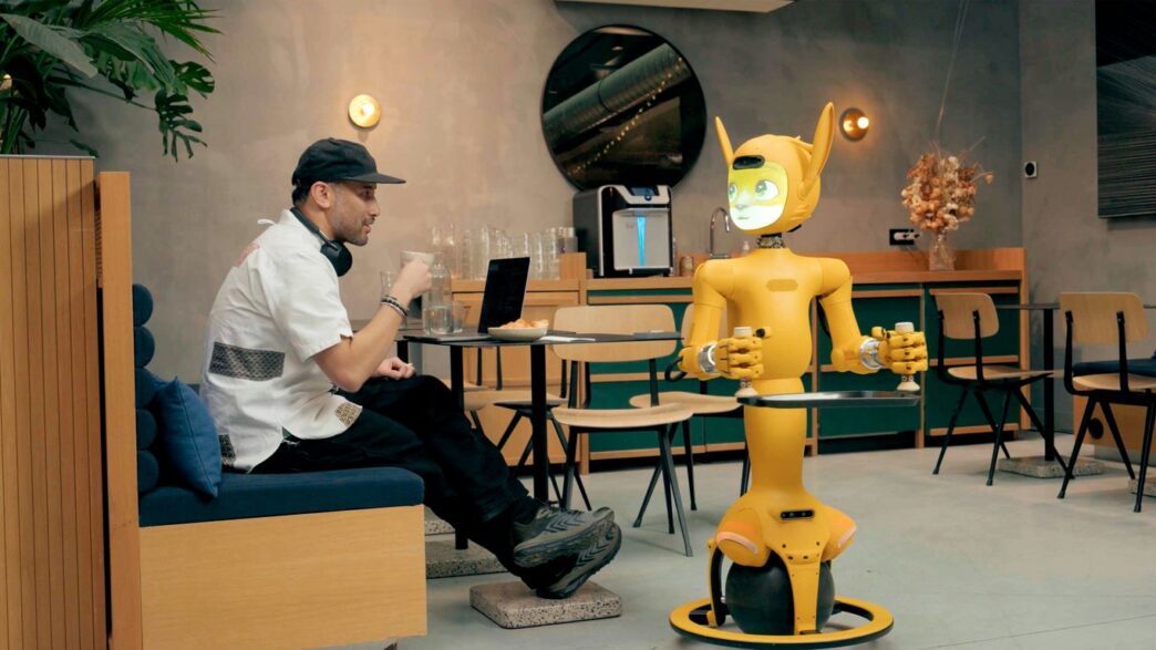 Man in cafe interacts with a yellow robot.