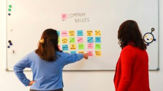 a couple of women standing in front of a white board