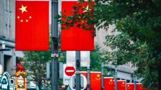 Chinese flags displayed on a street with trees.