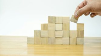 A person placing a block into a pile of wooden blocks