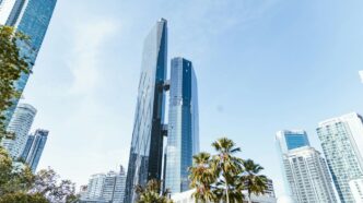 Modern skyscrapers and palm trees under a clear sky.