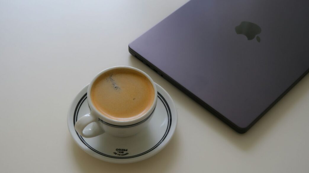 Espresso cup next to a closed laptop on white table