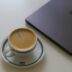 Espresso cup next to a closed laptop on white table