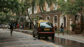 A yellow taxi and people on a wet street.