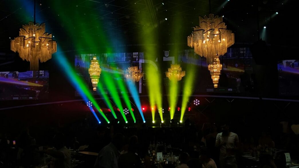 Stage lights illuminate an event with chandeliers.