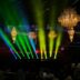 Stage lights illuminate an event with chandeliers.