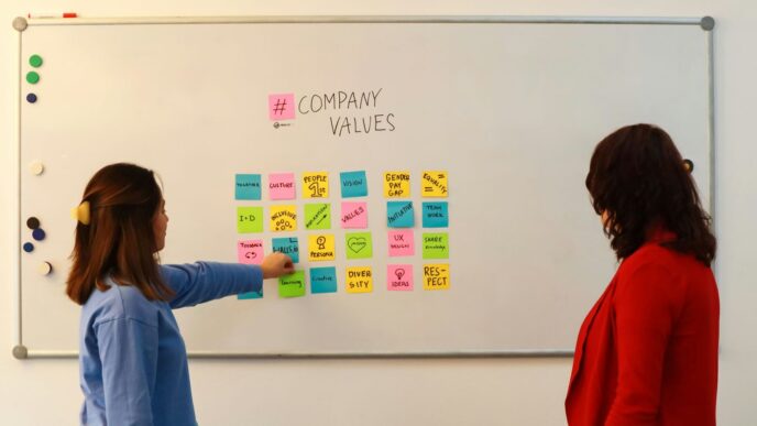 two women standing in front of a white board with sticky notes on it