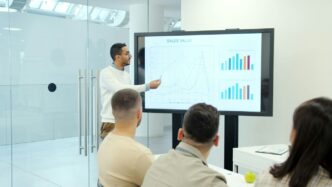 Man presenting charts on a large screen to audience.