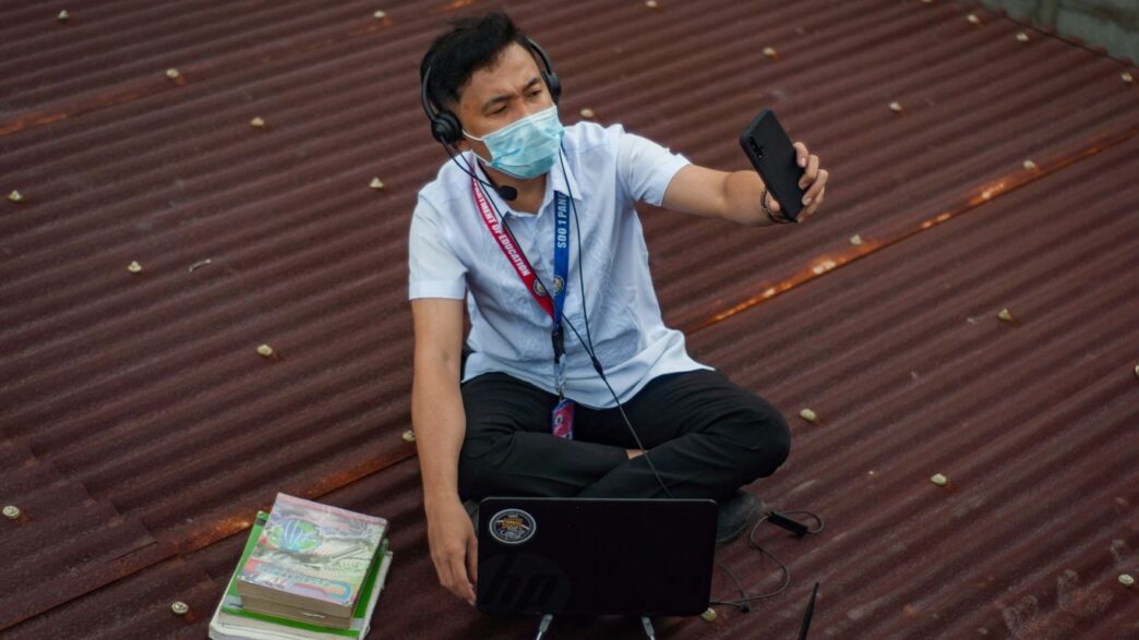 a man sitting on the ground with a laptop wearing a face mask