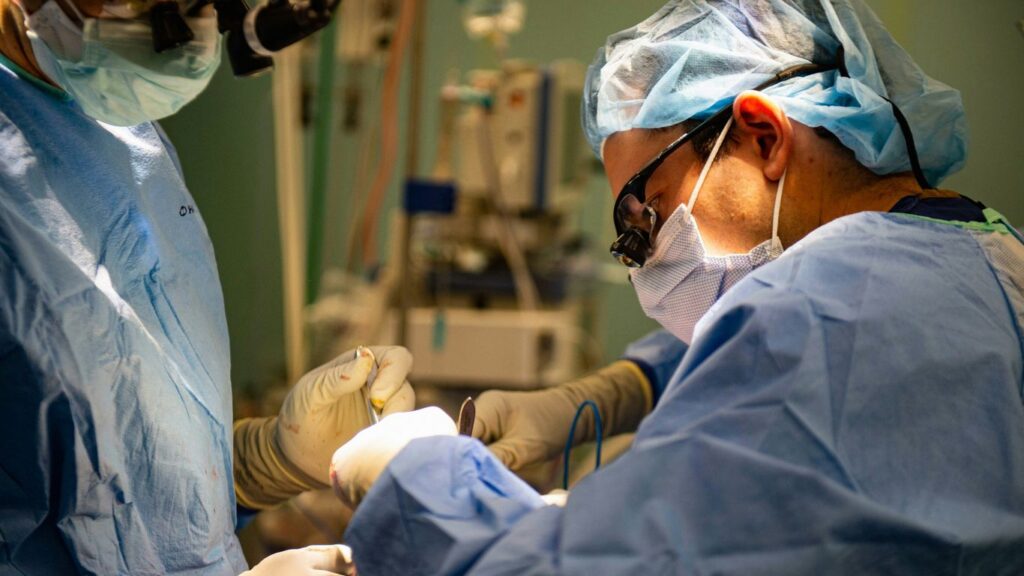 Surgeons in sterile gowns performing a medical operation.
