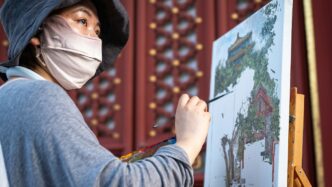 Woman painting a landscape with traditional buildings
