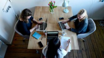 three women sitting around table using laptops