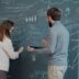 Two people collaborating on a chalkboard with diagrams.