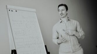Man standing next to a whiteboard with notes.