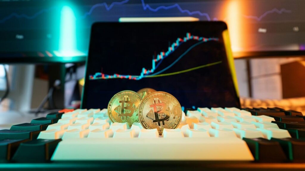 Bitcoin coins rest on a keyboard with stock charts.