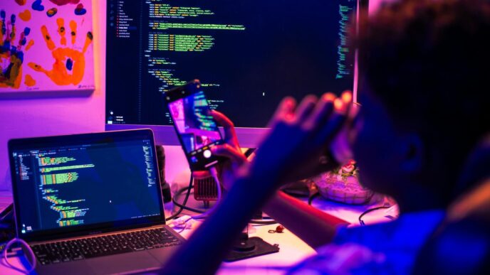 Person coding on multiple screens at night.