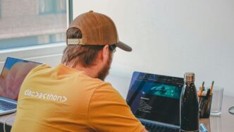 Man in a baseball cap coding on laptops