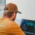 Man in a baseball cap coding on laptops
