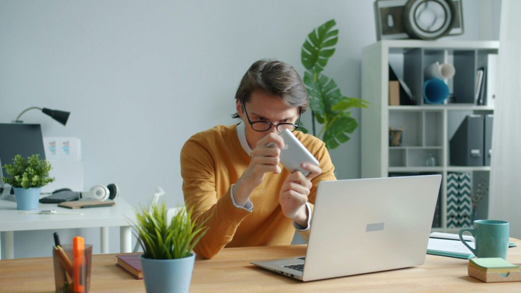 Man in yellow sweater drinking from mug at desk