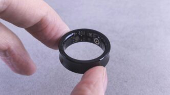 Fingers hold a black smart ring with circuits visible.