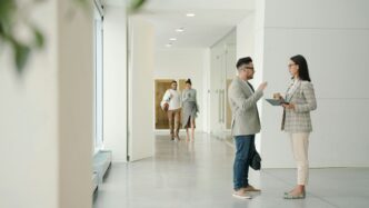 Two people talking in a modern office hallway.