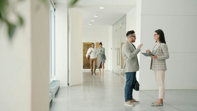 Two people talking in a modern office hallway.