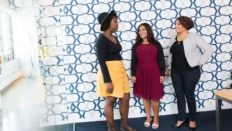 three standing women talking to each other