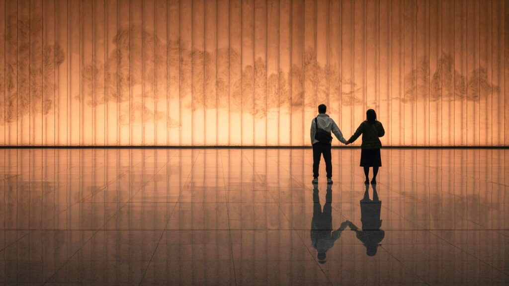Couple holding hands in front of illuminated wall