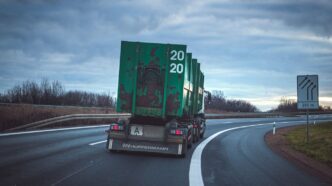 green freight truck passing by a winding road