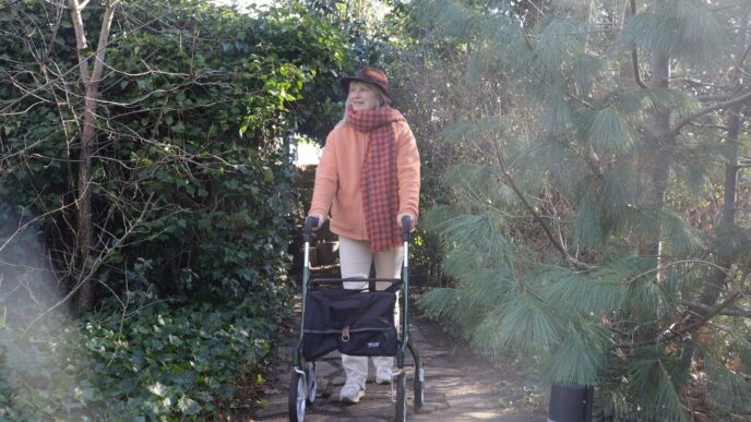 Elderly person with walker on a garden path.