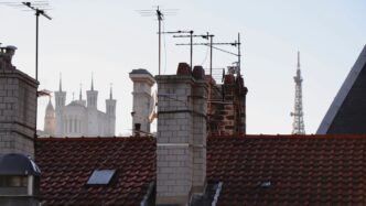 Rooftops and chimneys with distant cityscape and tower.
