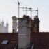 Rooftops and chimneys with distant cityscape and tower.