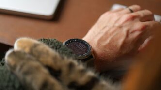 A hand working while a cat snuggles.