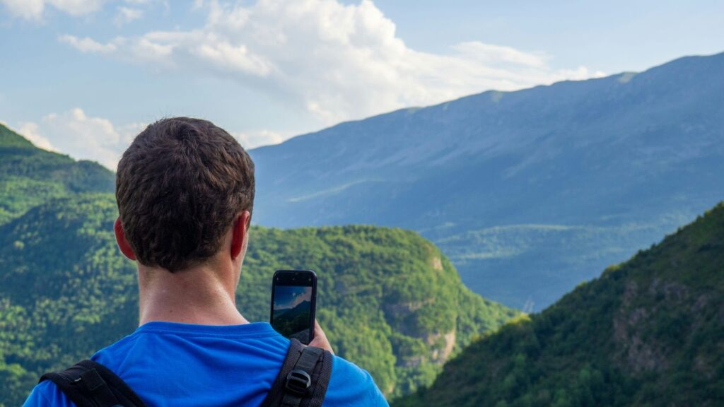 A man taking a picture of mountains with his cell phone