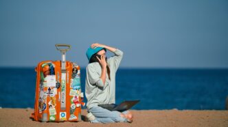 a person sitting on a beach with a suitcase and a laptop
