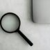 Magnifying glass sits near a laptop on a table.