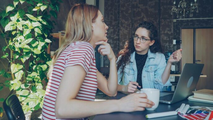 Two women are discussing something over a laptop.