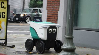 A small delivery robot with googly eyes on a sidewalk.