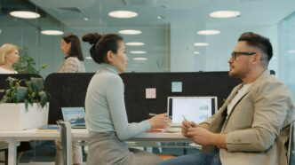 Two colleagues discussing work at their desks.