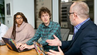 three people, one woman and two men, on laptops in a boardroom